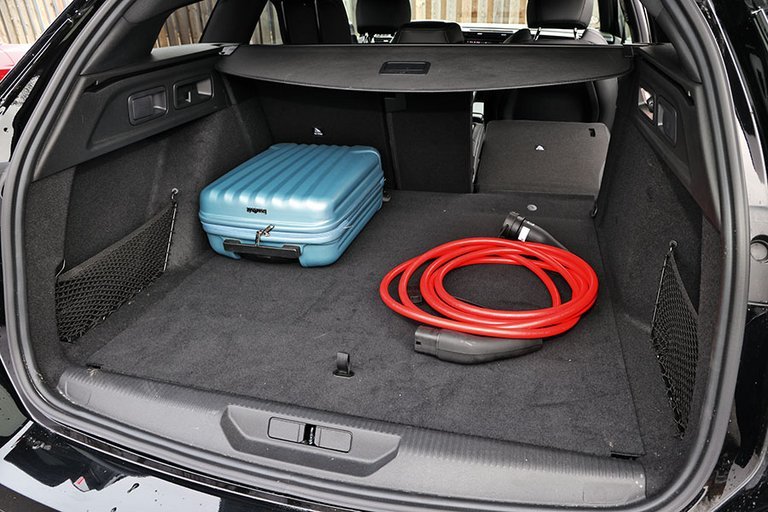 Bagagerum med blå kuffert og røde kabler i en Peugeot E-308