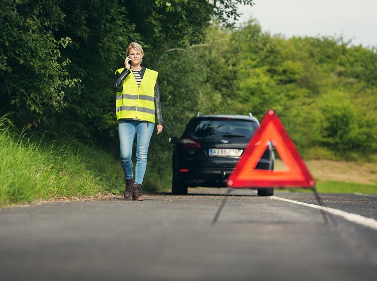 Advarselstrekant placeret bag bil, som holder i siden på en vej.
