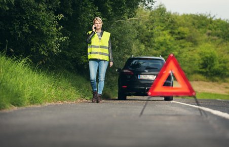 Advarselstrekant placeret bag bil, som holder i siden på en vej.