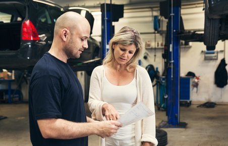 Kvinde taler med mekaniker på et værksted.