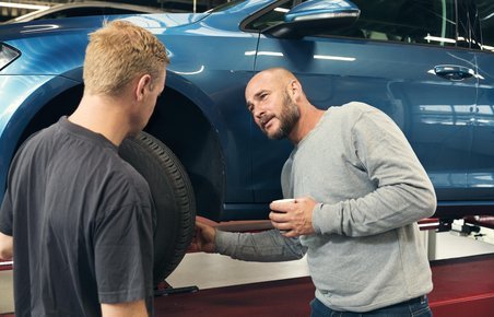 To mænd er ved at undersøge bremser på en bil, der er på værksted. 