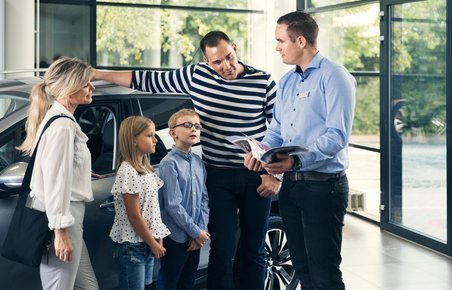 Familie i butik, som sælger biler. Bilsælger viser et katalog frem for familien. 