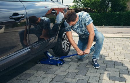 Mand er ved selv at skifte hjul på sin bil i en indkørsel.