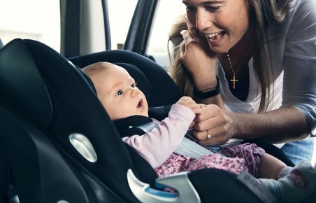 Mor kigger til baby, som sidder i autostol i en bil. 
