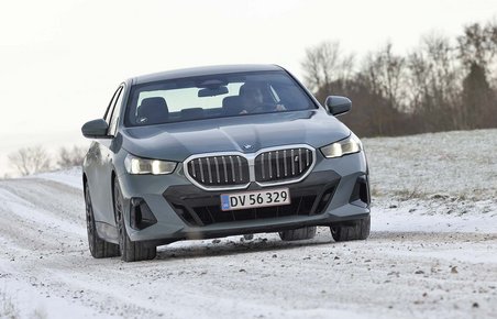 En BMW i5 elbil set forfra kører på en snedækket vej i et snedækket landskab.