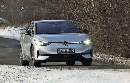 En sølvgrå VW ID.7 kører på en landevej med sne i forgrunden og træer i baggrunden